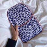 Hand holding navy blue festive waves quilted hot water bottle cover featuring a handprinted Japanese-inspired Seigaiha design, with contrasting red piping, against white bedding.