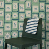 Folk Tales wallpaper in pistachio green with illustrated animal pattern shown in situ with chair for scale.
