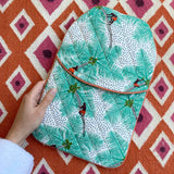 Person holding a quilted mint green hot water bottle cover featuring the handprinted Coconut Palm Pickers tropical print against a vibrant orange rug.